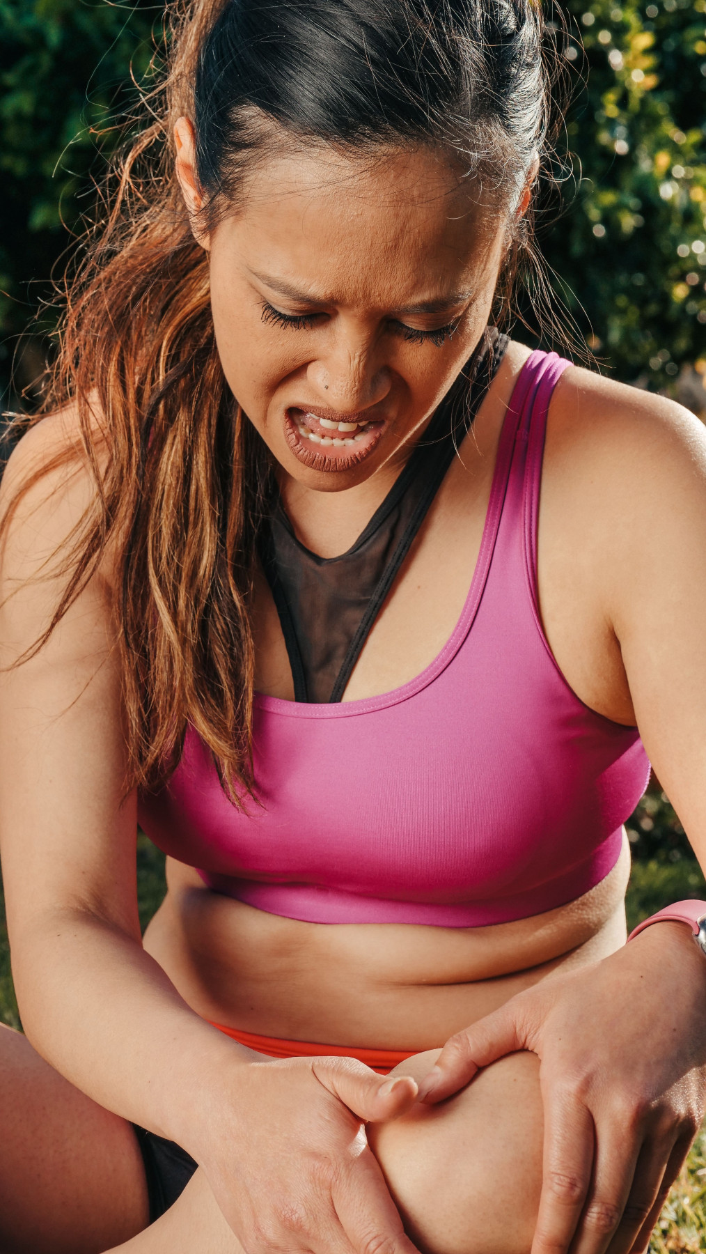 Woman in activewear holding her knee in pain during outdoor exercise, a common sign of a sports-related knee injury