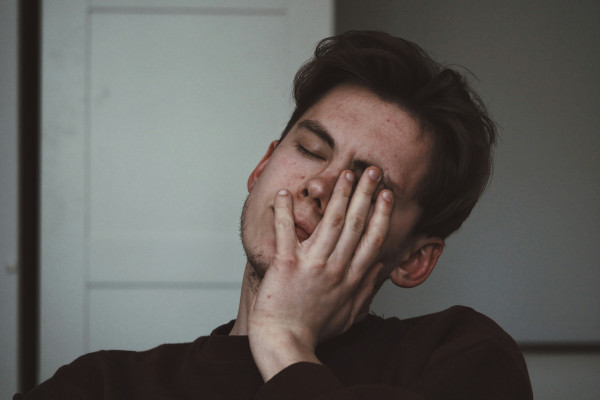 A man pressing his hand against his forehead in discomfort, showing the strain of a headache or migraine.