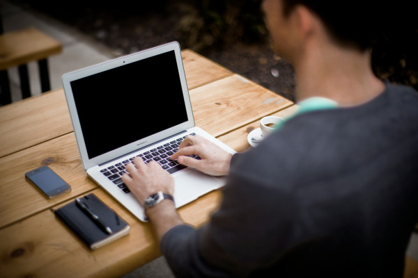 A man sitting slouched in front of a laptop, working at a desk.