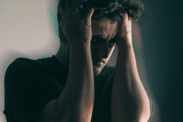 A man sitting with his head held in both hands, showing visible discomfort.