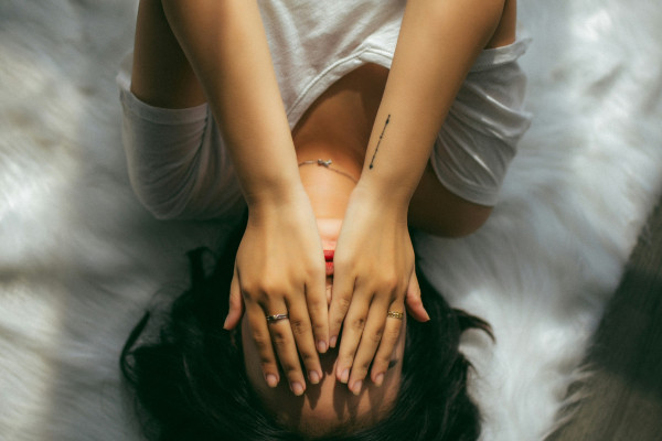 A woman holding both hands over her face, visibly in discomfort from head pain.