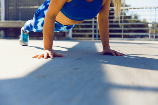 A woman holding a plank position outdoors on a paved road.