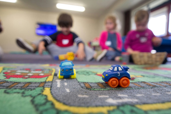 Children playing with toy cars on the floor, engaged in imaginative play.