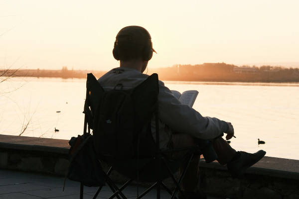 A person sitting by the water at sunset, reading peacefully.