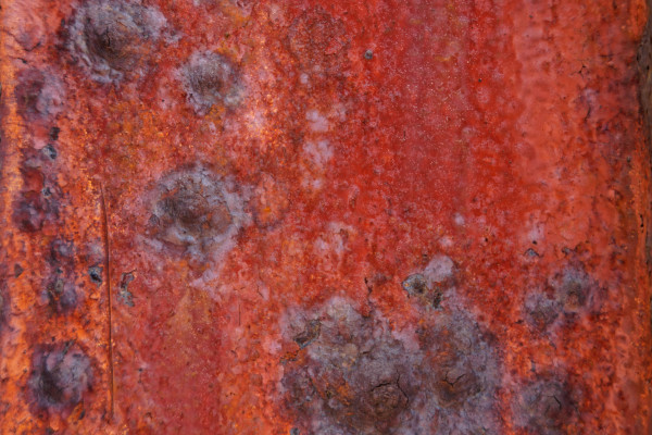 Close-up of a heavily corroded, rusted metal surface with small holes, illustrating decay without ongoing maintenance
