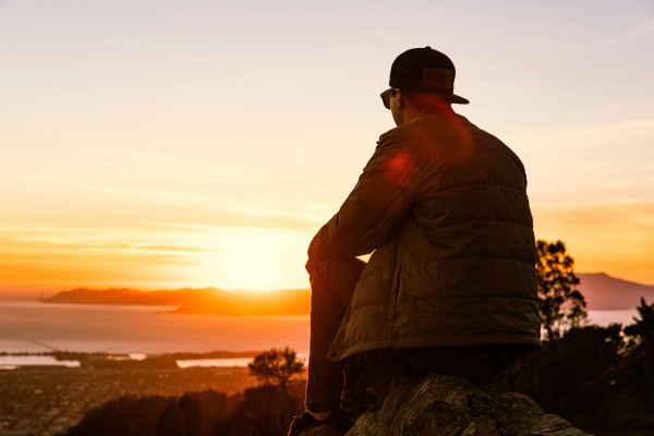 A man sitting on a rock, looking out at the sunrise.