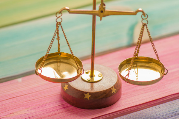 A small gold balance scale resting on a colourful wooden surface, symbolising equilibrium between two sides.