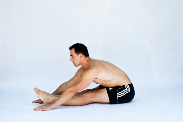 A man sitting on the floor performing a hamstring stretch, reaching toward his toes