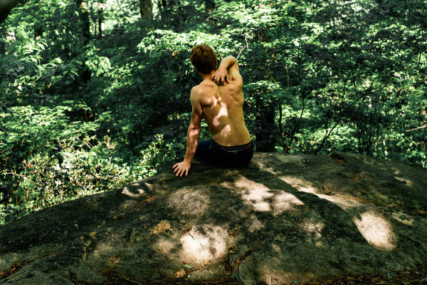 A man sitting outdoors, holding his lower back in discomfort.