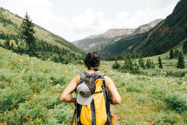 A person hikes through green mountain terrain with a backpack, representing an active, ongoing approach to health