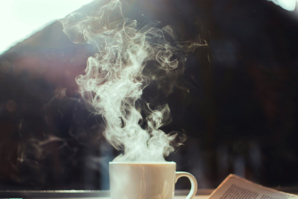 A cup of coffee and an open book resting on a sunlit window sill.