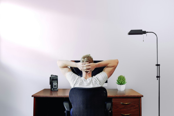 Man sitting slumped at a computer desk with his head in his hands, illustrating the poor sitting posture that can lead to lower back pain