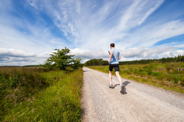 A man running along a grassy trail with hills in the background.