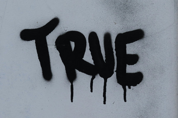 The word "true" spray-painted in large letters on a white wall.