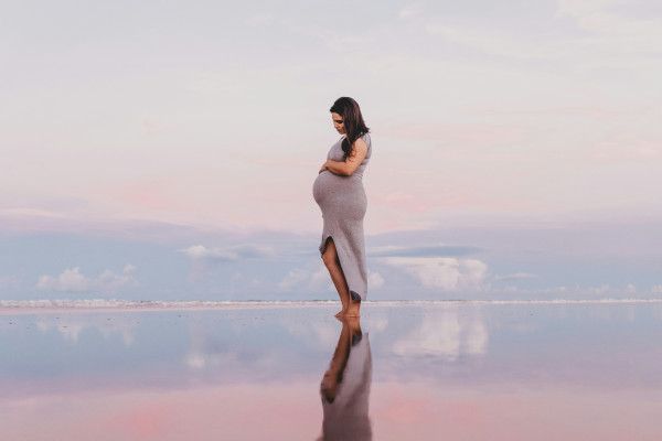 A pregnant woman standing calmly by still water, reflecting the sense of relaxation pregnancy massage aims to support