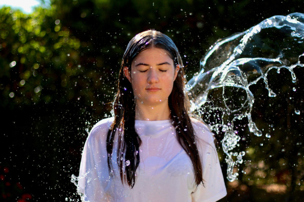 A woman with water splashing across her face, eyes closed.