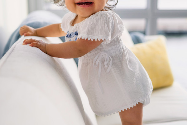 A smiling toddler girl learning to walk by leaning on a sofa