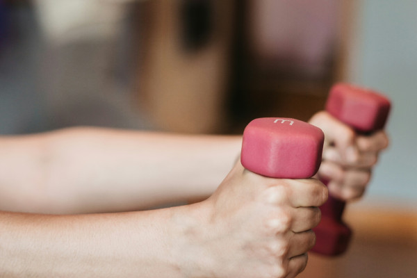 A person holds a pair of light dumbbells, demonstrating grip and hand strength during exercise.