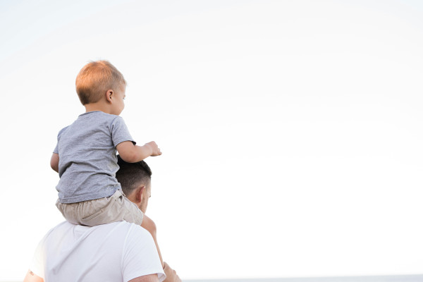 A man carries a young boy on his shoulders outdoors, representing the everyday responsibilities people carry for those who depend on them.