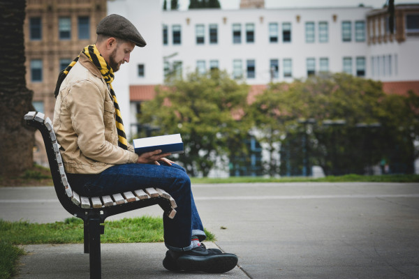 A man sitting on a park bench, reading a book outdoors.