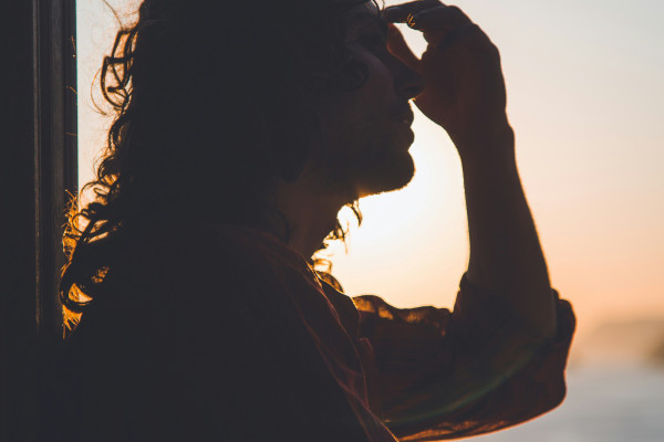 Silhouette of a person pressing their hand to their forehead in discomfort, evoking the head pain and light sensitivity associated with migraines