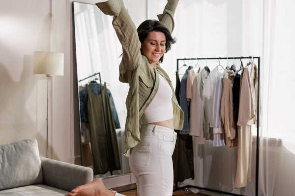 Woman smiling with arms raised overhead, stretching in a bright bedroom