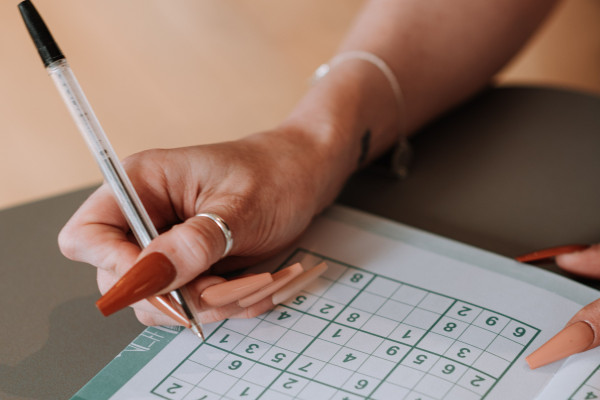 Close-up of a hand solving a sudoku puzzle in a book with a pen.