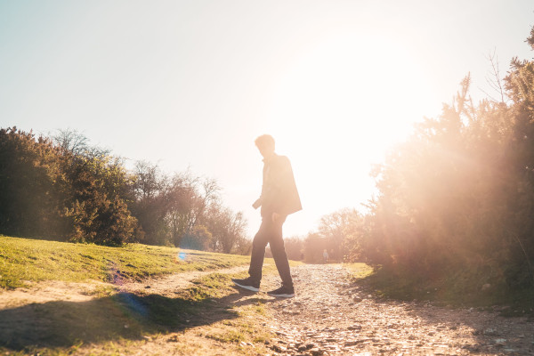 Silhouette of a person walking along a sunlit path at sunset