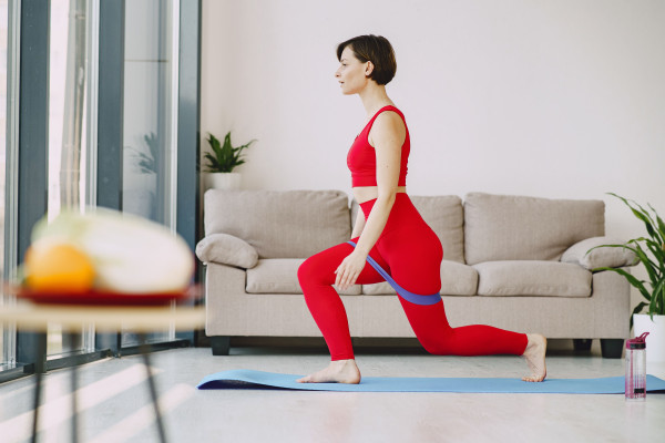 Woman in red sportswear stretching indoors with a resistance band