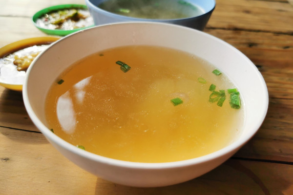 Homemade soup garnished with scallions in a bowl on a wooden table