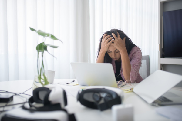 Woman sitting at a desk with a laptop, visibly frustrated and tense in a modern office.