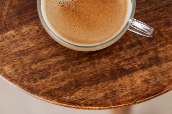 A cup of coffee on a rustic wooden table, viewed from above, steam rising gently from the surface
