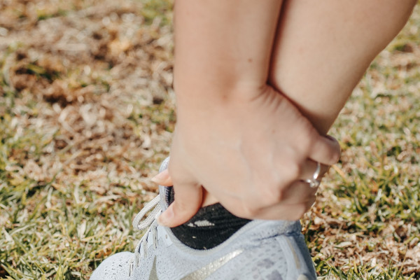 Close-up of a person holding their ankle in a sneaker, indicating pain or injury