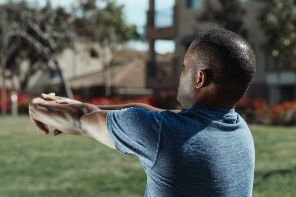Man stretching his arms outdoors in a park surrounded by greenery
