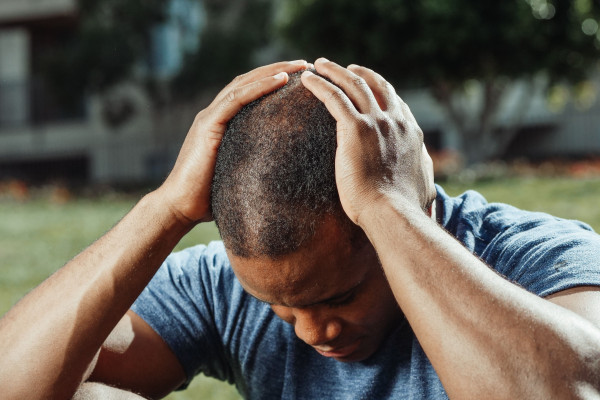 Man sitting outdoors with his head in his hands, showing the visible discomfort of pain.