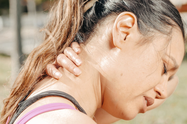 Close-up of a woman holding the back of her neck outdoors, showing signs of pain