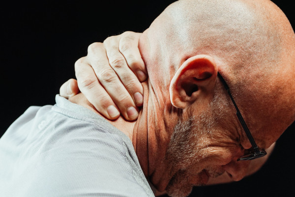Close-up of a man holding the back of his neck, showing signs of pain or discomfort