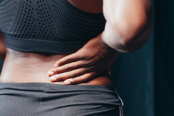 Close-up of a woman in athletic wear holding her lower back outdoors, showing signs of discomfort