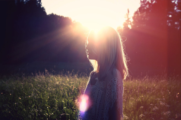 Silhouette of a woman standing in a sunlit field at sunset