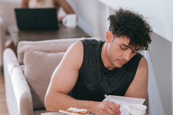 A young man writing in a journal with coffee at a cosy café table