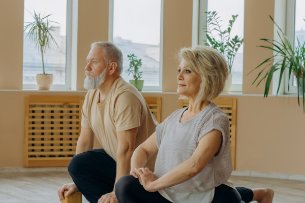 Senior couple sitting cross-legged in a stretching pose during an indoor yoga session