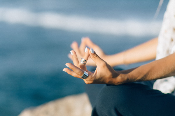 Close-up of a person meditating by the seaside, hands resting calmly.