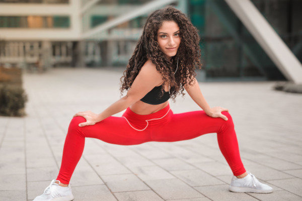 Woman in red athletic wear stretching in a wide lunge position outdoors