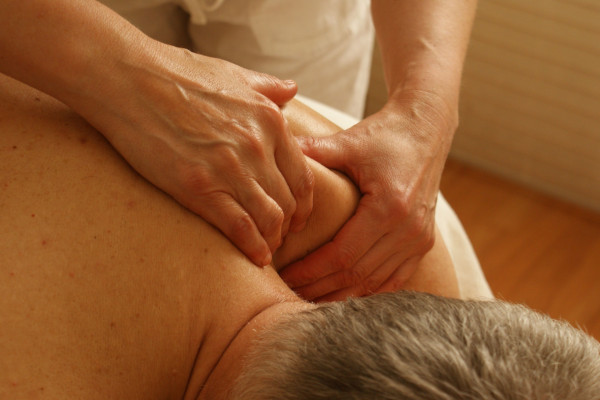 Close-up of a therapist's hands massaging a man's shoulder and upper back to relieve tension.