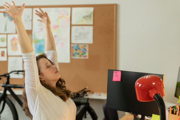 Woman pausing at her office desk to stretch her back and shoulders during a work break