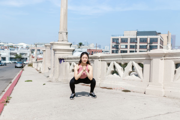 Woman performing a squat exercise outdoors on a city sidewalk