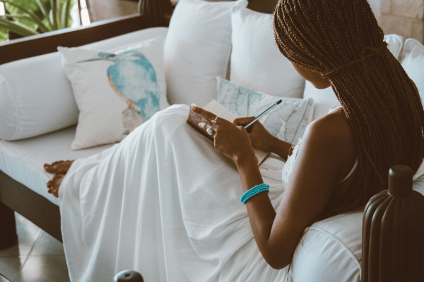 Woman sitting calmly on a sofa, writing reflectively in a notebook