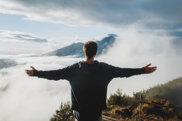 "Man standing on a misty mountain cliff with arms outstretched and chest open