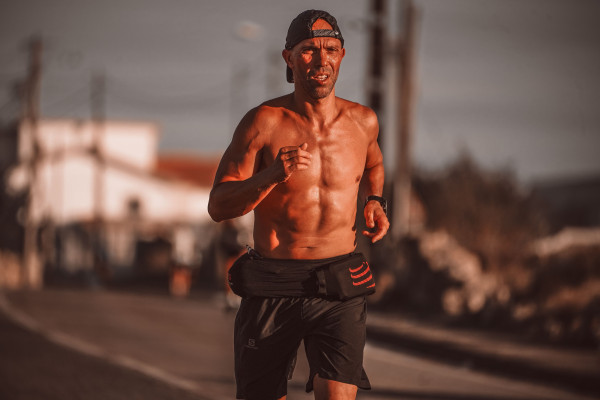 Muscular man running along a road at sunset, wearing a cap and shorts