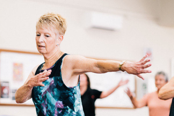 Senior woman smiling and moving confidently in an indoor fitness class.